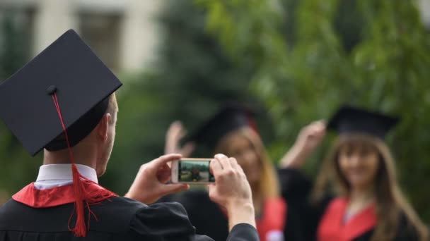 Hombre filmando mejores amigos lanzando gorras de graduación en el aire y posando para la cámara — Vídeo de stock