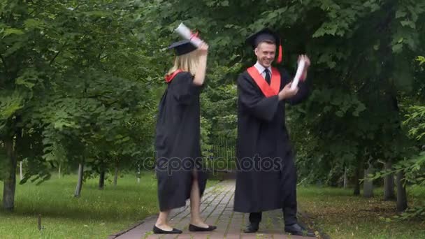 Divertidos graduados en vestidos académicos bailando y tonteando después de la graduación — Vídeos de Stock