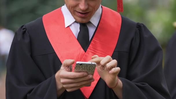 Hombre graduado de la universidad comprobar el correo electrónico en el teléfono inteligente, haciendo signo de la mano éxito — Vídeos de Stock