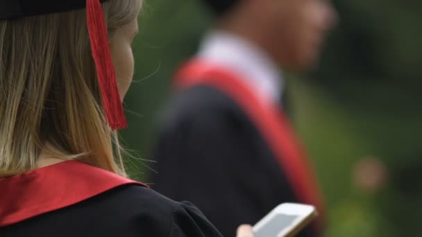 Close-up ของบัณฑิตหญิงในชุดนักศึกษาอ่านข้อความบนสมาร์ทโฟน — วีดีโอสต็อก