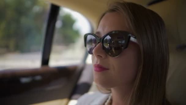 Jovem mulher de óculos de sol sentada no banco de trás, desfrutando de vista da janela, viagem — Vídeo de Stock