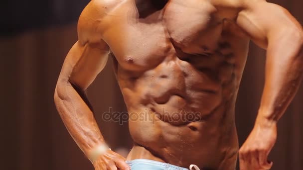 Мужчина бодибилдер демонстрирует загорелое мышечное тело на соревнованиях по фитнесу — стоковое видео