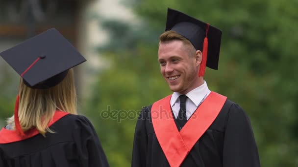 Vrolijke man en vrouw in academische jurk praten en lachen, gelukkig afgestudeerden — Stockvideo