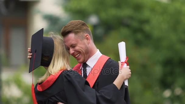 Opgewonden mannelijke en vrouwelijke universitair gediplomeerden uitwisselen Gefeliciteerd, knuffelen — Stockvideo