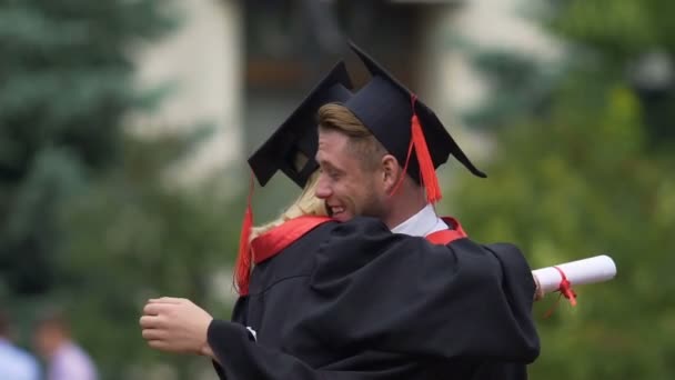 Amigos do sexo masculino e feminino abraçando, segurando diplomas de ensino superior em mãos — Vídeo de Stock