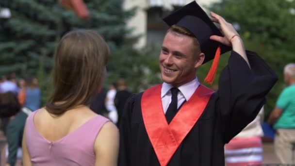 Веселый мужчина-выпускник улыбается и надевает свою академическую шапку на младшую сестру — стоковое видео