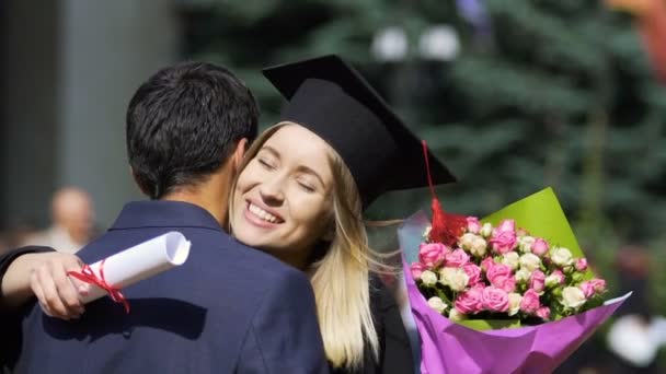 Feliz mujer abrazando calurosamente al hombre con ramo de flores, ceremonia de graduación — Vídeos de Stock