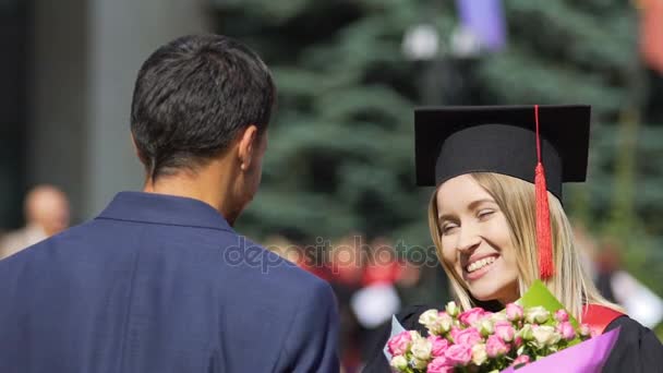 Счастливая выпускница получает поздравления и цветы от парня — стоковое видео
