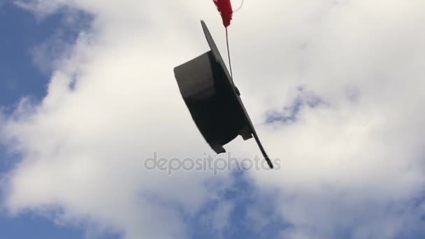 Gorra académica con borla lanzada en el aire volando sobre fondo azul del cielo — Vídeos de Stock