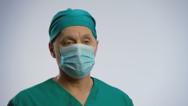 Уставший доктор-мужчина глубоко вздыхает, снимает медицинскую маску для лица, вытирает бровь — стоковое видео