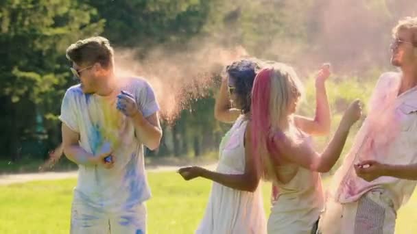 Giovane donna allegra che lancia colori holi al fidanzato, gli amici si divertono — Video Stock