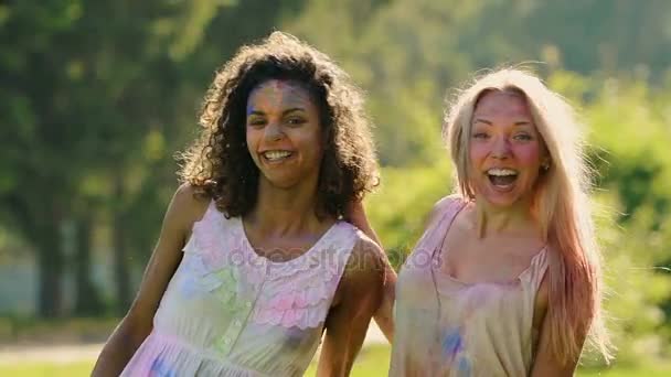 Belles amies couvertes de peinture colorée étreignant, souriant à la caméra — Video