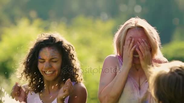 Amigos salpicando agua en dos mujeres jóvenes excitadas cubiertas de polvo de color — Vídeo de stock