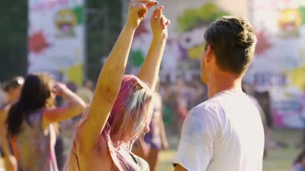 Verleidelijke jonge vrouw dansen op vriendje, paar bedekt met holi kleuren — Stockvideo