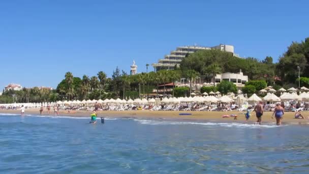 Moltitudine di persone che si rilassano sulla spiaggia di sabbia con vista sul lussuoso hotel orientale — Video Stock