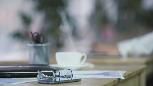 事務作業、ラップトップ、スマート フォン、テーブルに横になっている眼鏡。職場 — ストック動画