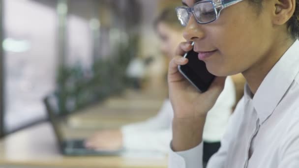 Gemengd ras zakenvrouw praten over smartphone in kantoor, werk dag routine — Stockvideo