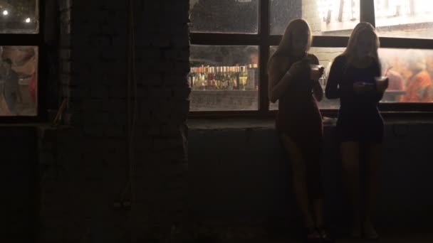 Twee mooie vrouwen drinken van cocktails, browsen op smartphones bij nightclub — Stockvideo