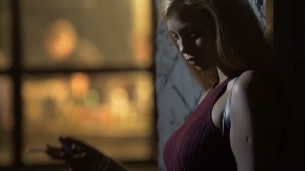 Blonde Dame im langen Kleid genießt das Rauchen und steht in der Nähe eines Nachtclubs, schlechte Angewohnheit — Stockvideo