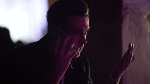 Эмоциональный молодой мужчина разговаривает по телефону в ночном клубе, ссорится, расстается — стоковое видео