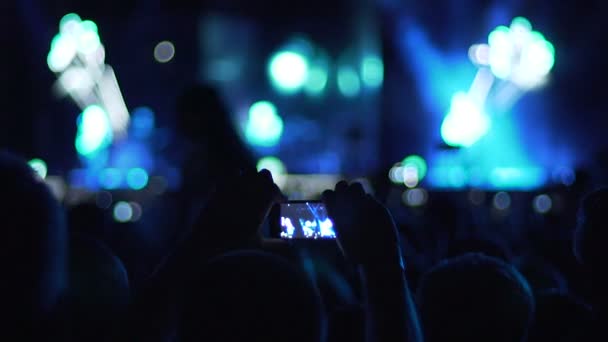 Hombre usando gadget cámara para filmar vídeo de concierto, siluetas de audiencia — Vídeos de Stock