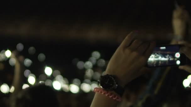 Mains de jeune femme filmant sur gadget foule de personnes avec des lumières dans l'obscurité 