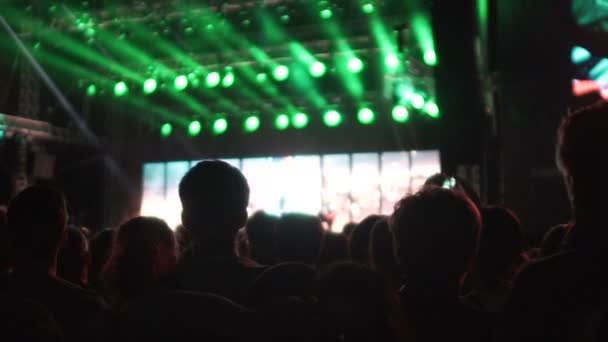 Siluetas de multitud en la sala de conciertos oscura, gente mirando en el escenario iluminado — Vídeo de stock