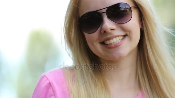 Hermosa chica rubia con la piel perfecta sonriendo a la cámara, gafas de sol de vez en cuando — Vídeo de stock