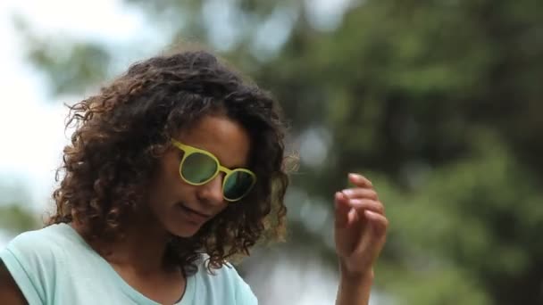 Χαριτωμένο κορίτσι biracial κάνοντας μάτι επαφή βάζοντας κάτω γυαλιά ηλίου ενώ ο χορός — Αρχείο Βίντεο