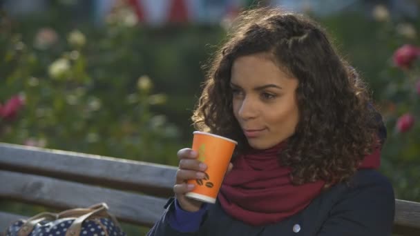 Замороженная женщина пьет кофе, чтобы согреться, ждет друзей, сидящих на скамейке — стоковое видео