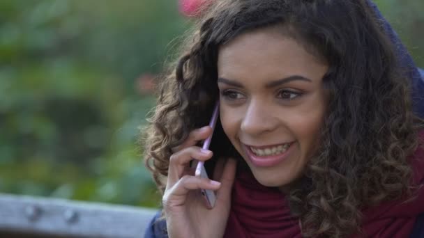 Щаслива змішана раса жінка розмовляє через смартфон на відкритому повітрі, посміхаючись, закінчуючи дзвінок — стокове відео