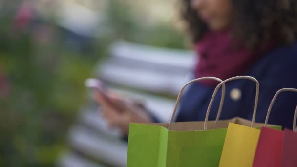 Jeune femme faisant du shopping en ligne sur smartphone assis sur un banc à l'extérieur — Video