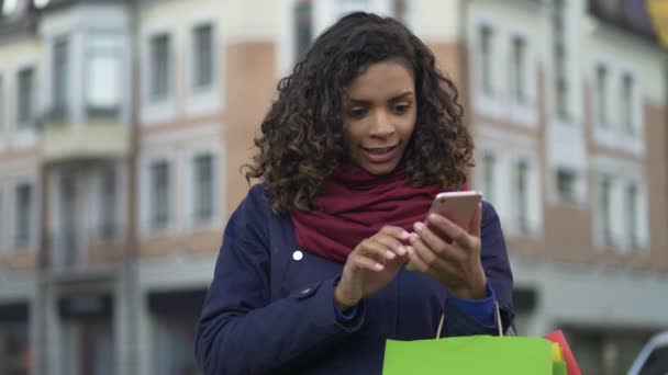 Mujer de raza mixta comprobando aplicaciones de tienda en línea en el teléfono inteligente moderno, compras — Vídeos de Stock