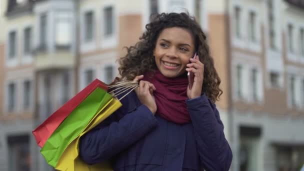 Женщина с сумками звонит подругам, чтобы рассказать о скидках в магазинах — стоковое видео