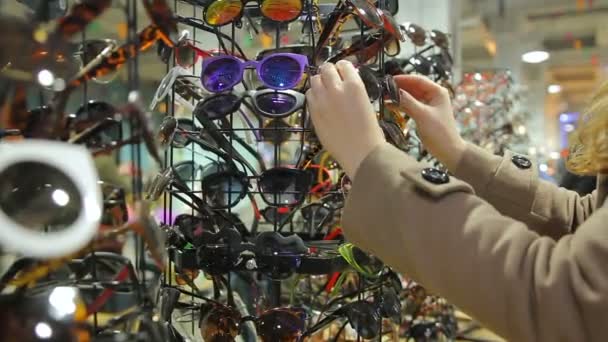 Lady confused with large choice of sunglasses on shopping stands at local market — Stock Video