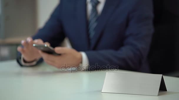 Üzletember görgetés okostelefonon az irodában, üres névtábla sablon szöveg — Stock videók