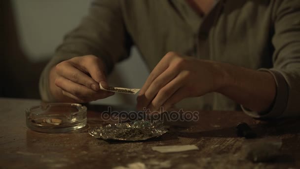 Молодой человек делает сигарету конопли, чтобы облегчить стресс, злоупотребление психоактивными препаратами — стоковое видео