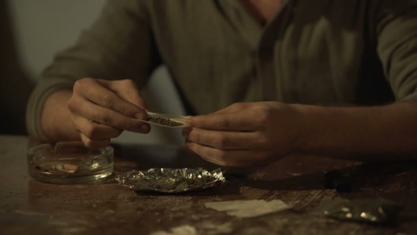 Чоловік залежний від куріння марихуани, що робить суглоб, кидаючи канабіс в папір — стокове відео
