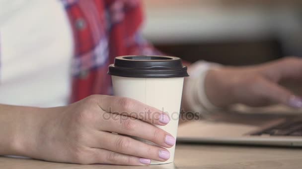 Young lady drinking coffee from paper cup and looking through newsfeed on laptop — Stock Video