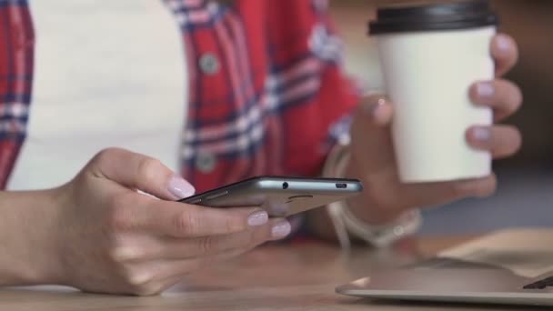 Manos de mujer joven deslizando fotos en el teléfono inteligente durante el descanso de café en la cafetería — Vídeo de stock