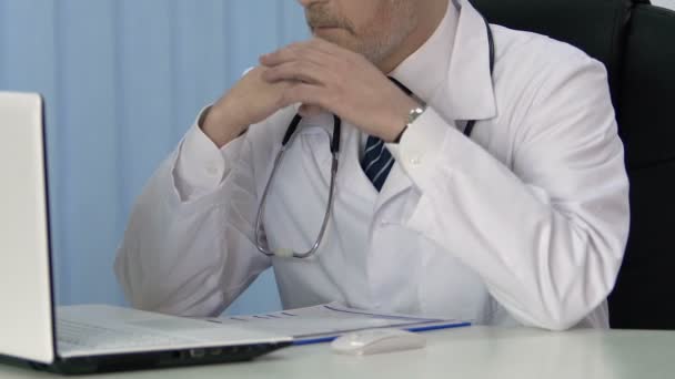 Medico di sesso maschile che lavora su laptop, inserendo dati nella cartella clinica per l'assicurazione — Video Stock