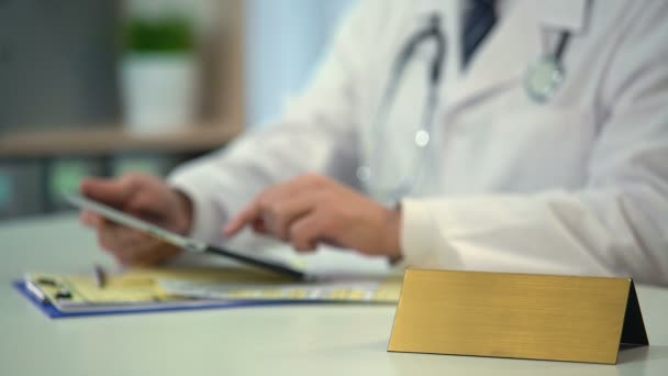 Practitioner checking clinical records on tablet, blank nameplate on table — Stock Video