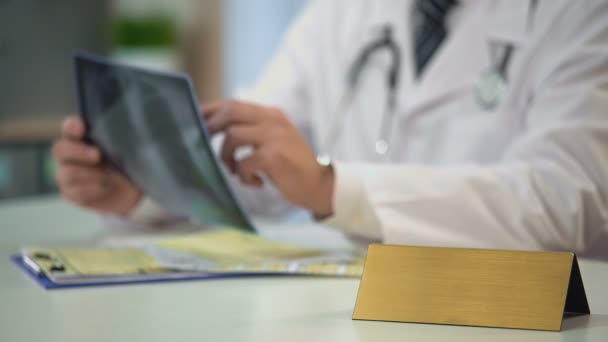 Врач мужского пола смотрит на рентген легких, пишет диагноз, табличка с бланком на столе — стоковое видео
