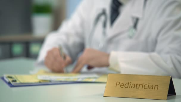 Pediatra que escreve prescrição na clínica, médico que preenche a documentação — Vídeo de Stock