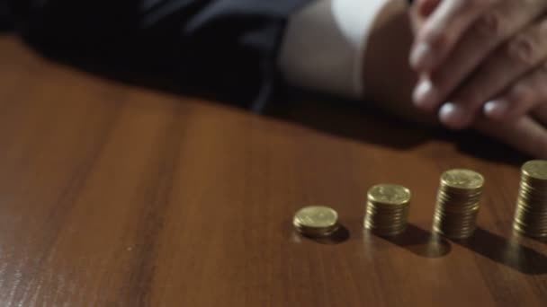 Кучи монет и песочного стекла на столе, вкладчик получает проценты по сбережениям — стоковое видео