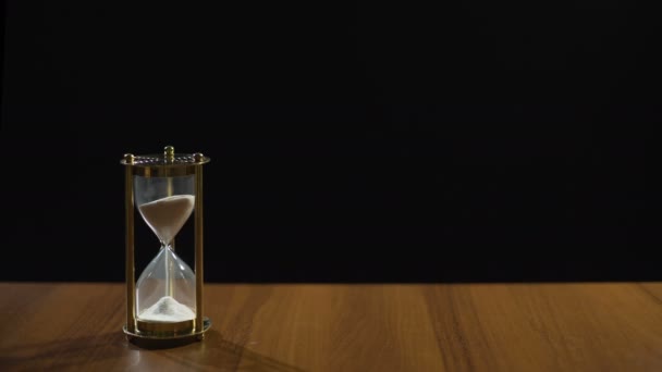Písek teče rychle přesýpací hodiny na stole černém pozadí, čas letí — Stock video