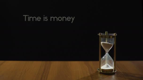 Tijd is geld, verstandig zin tegen zwarte achtergrond, zand stroomt in de zandloper — Stockvideo