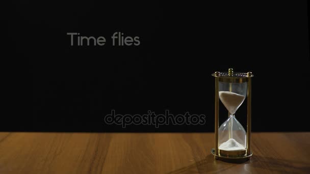 El tiempo vuela, frase sobre la transitoriedad de la vida, arena que fluye en reloj de arena en la mesa — Vídeo de stock