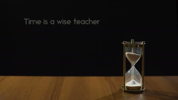 Tijd is verstandig leraar, de populaire uitdrukking over ervaring, de zandloper op tafel — Stockvideo