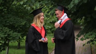 Diploma tutarak ve parkta gelecek hakkında konuşmak gülümseyen mezunları heyecanlı